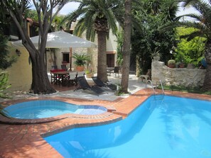 Ein Schwimmbecken mit Fliesen umgeben von Palmen und einer Terrasse mit Gartenmöbeln.