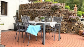 Un patio al aire libre con una mesa, sillas, un muro de piedra y una estatua.