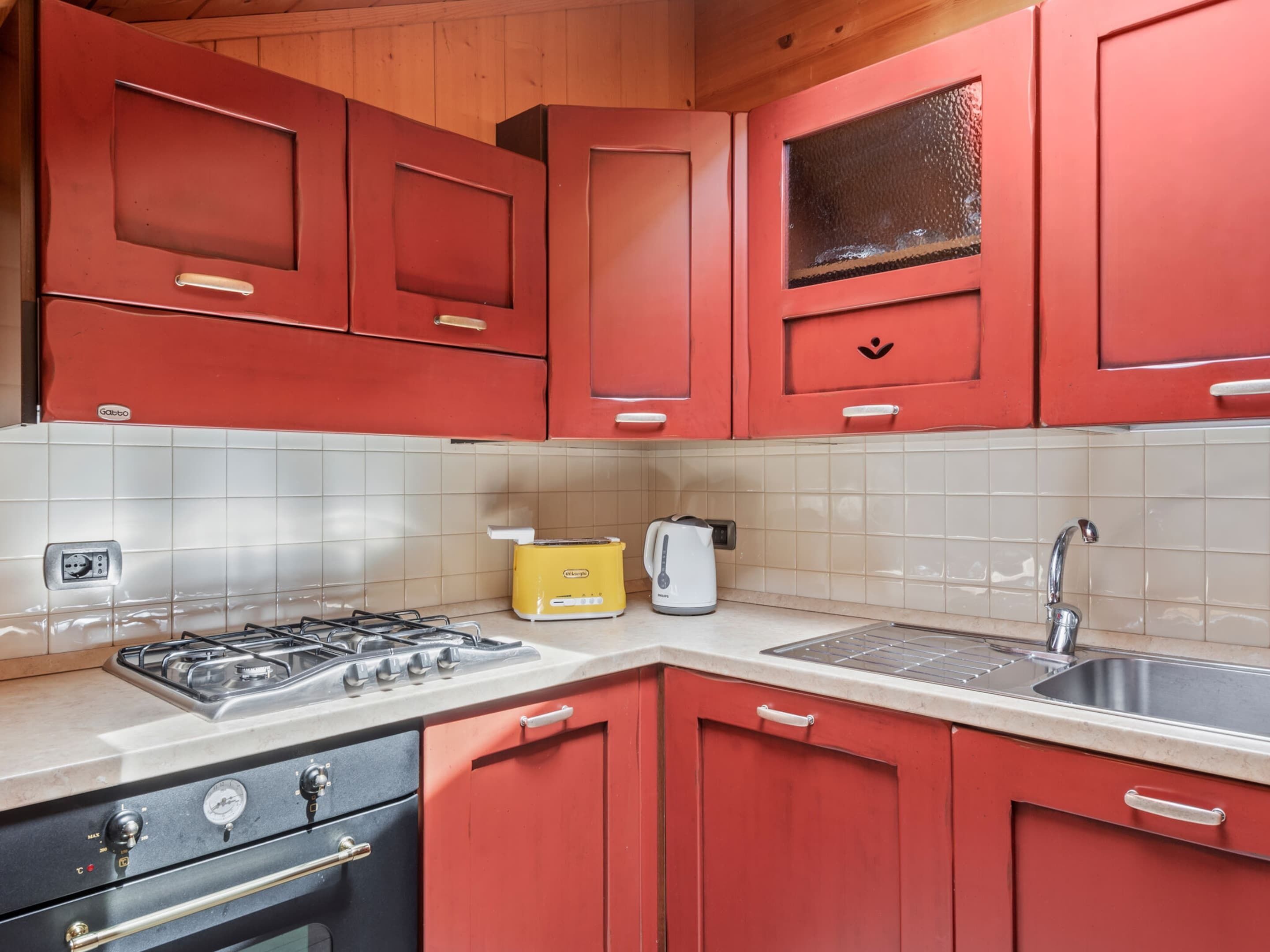A kitchen with red cabinets, a gas stove, a yellow toaster, and a sink.