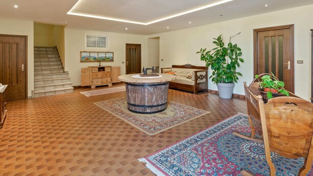 A spacious living area with a central round table, a sofa, a wooden cabinet, and a staircase leading to an upper floor.