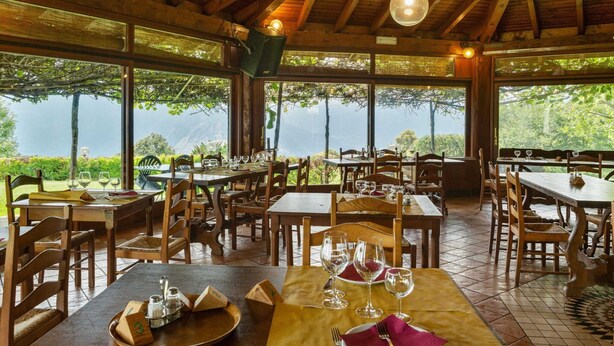 A restaurant with wooden tables and chairs, large windows offering a view of the outdoors, and hanging pendant lights. - Farmhouse in Verbania With Lake Views (Verbania)