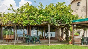 A covered outdoor seating area with chairs and a table, surrounded by greenery and a building. - Farmhouse in Verbania With Lake Views (Verbania)