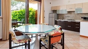 A modern kitchen with a gas stove, a refrigerator, and wooden cabinets. There is a glass table with floral chairs in the dining area. - Holiday Home in Bardolino With Pool & Lake Views (Bardolino)