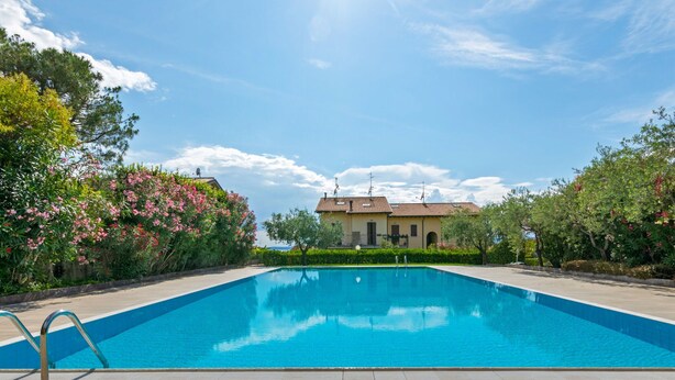 A rectangular swimming pool with a tiled deck, surrounded by lush greenery and flowering plants. - Holiday Home in Bardolino With Pool & Lake Views (Bardolino)