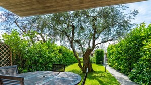 A patio with a round table and chairs, surrounded by lush greenery and a tree. - Holiday Home in Bardolino With Pool & Lake Views (Bardolino)