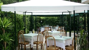An outdoor dining area with tables and chairs under a white canopy, surrounded by greenery. - Seaside Escape in Giannella (Orbetello)