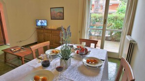 A dining area with a table set for two, featuring plates of food, a glass of wine, and a vase with flowers. - Seaside Escape in Giannella (Orbetello)