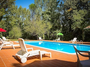 A swimming pool with white lounge chairs and a red umbrella. - Belvilla by OYO Holiday Home With Pool (Montecatini Val di Cecina)