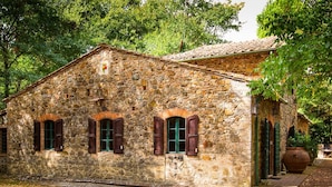 Un edificio de piedra con techo de tejas, ventanas arqueadas y una maceta grande al frente.