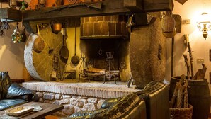 Un interior rústico con chimenea de piedra, asientos de cuero y diversos utensilios de cocina exhibidos en estantes.
