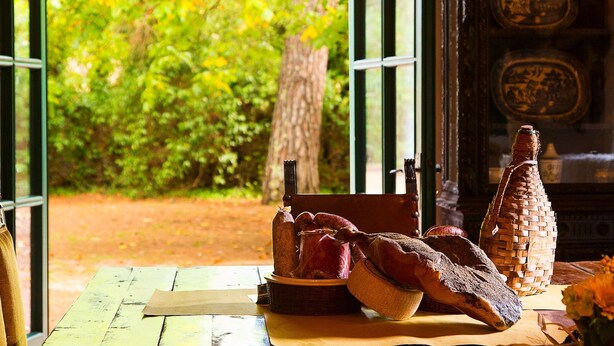 Una mesa de madera rústica con pan, una cesta tejida y una jarra de cerámica.