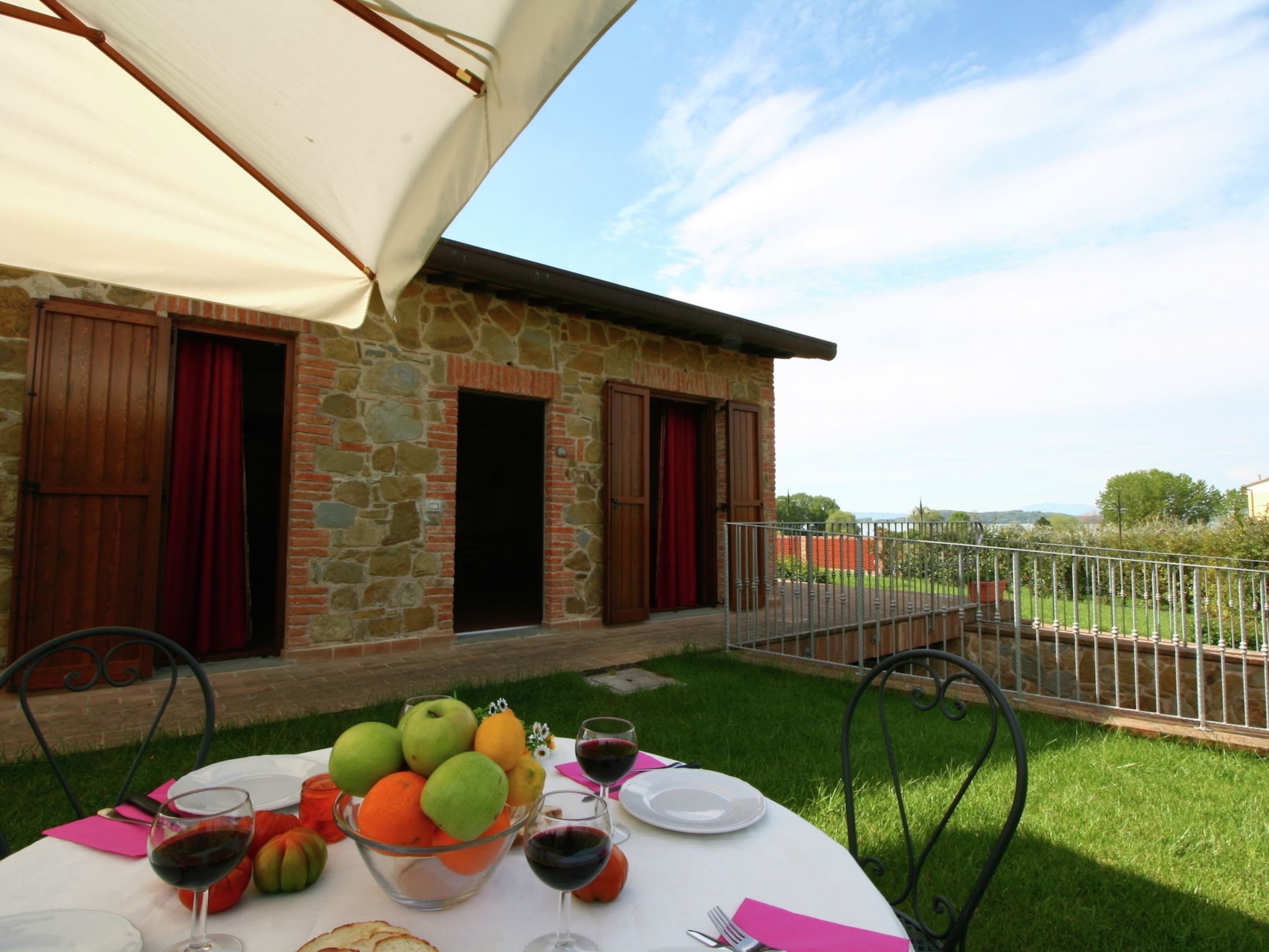 A stone building with a balcony, a table set for a meal with fruit and wine, and a view of the countryside.