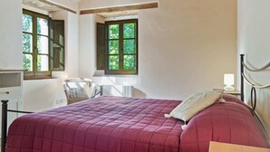 A bedroom with a large bed, a chair, a desk, and a window with a view of greenery. - Belvilla by OYO Villa Carina (Serra San Quirico)