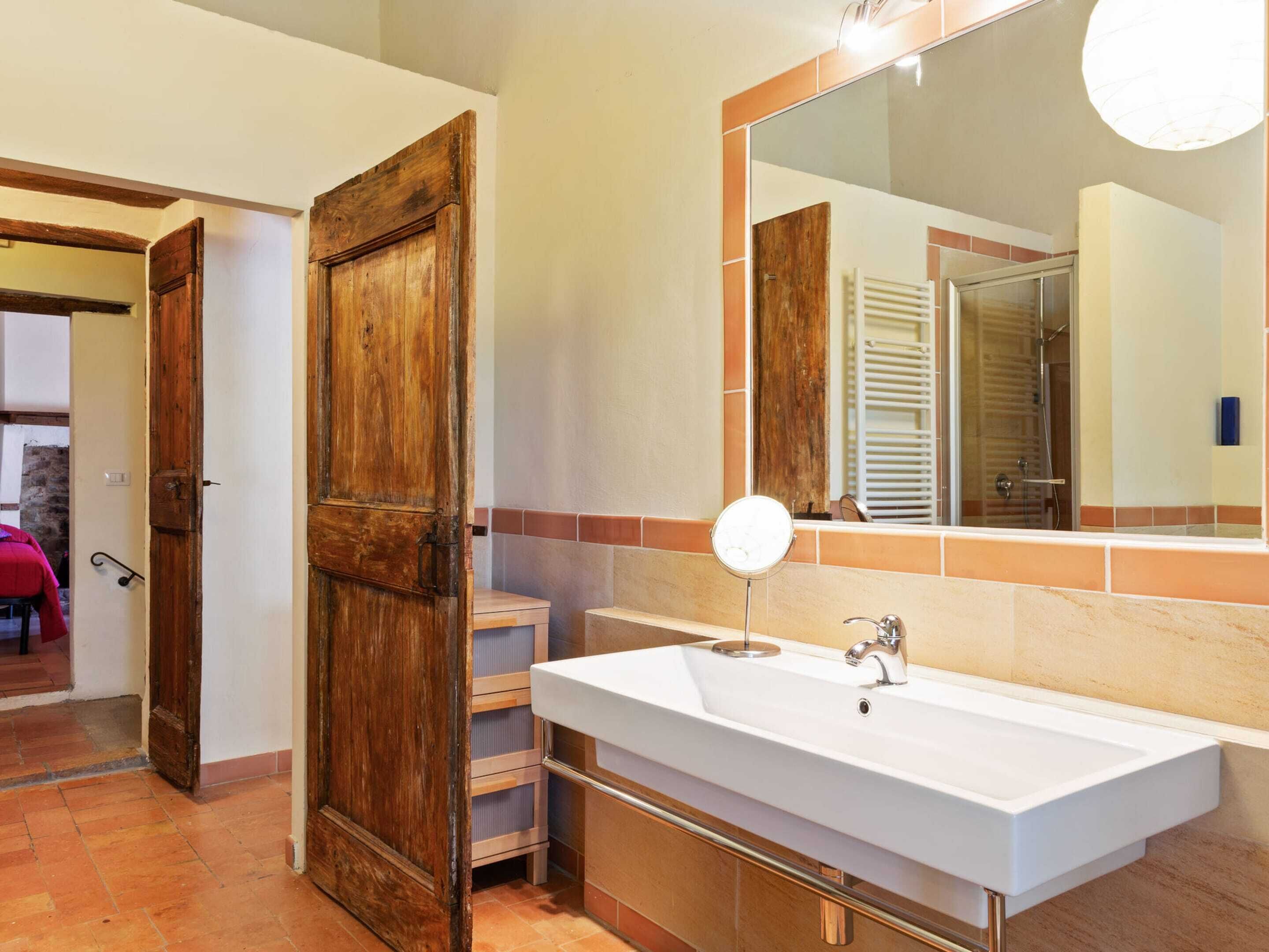 Une salle de bain avec une porte en bois, un lavabo blanc et un grand miroir.