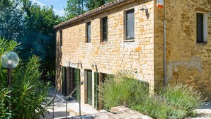 A stone building with a tiled roof, green shutters, and a small garden area with plants and a lamp post. - Belvilla by OYO Villa Carina (Serra San Quirico)
