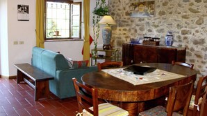 A cozy living room with a blue sofa, a wooden dining table with chairs, and a stone wall. - Rustic Farmhouse Living Vinci's Treasures (Vinci)