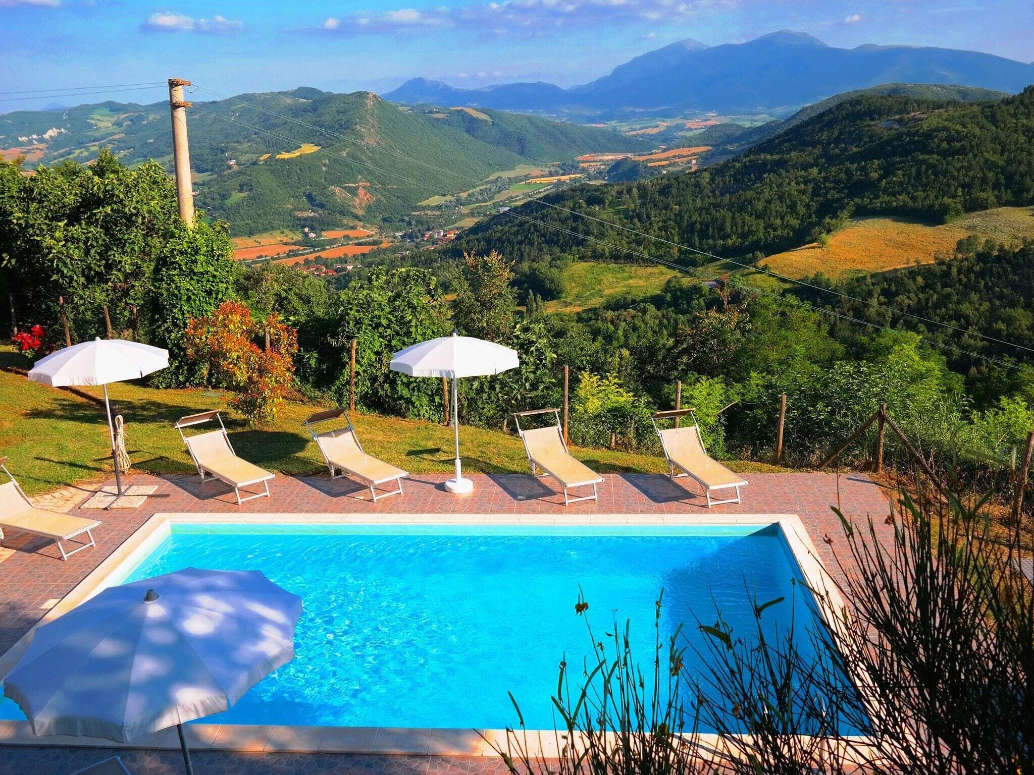 A swimming pool with lounge chairs and umbrellas, surrounded by lush greenery and a view of distant mountains.