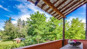 Un balcon doté d’une table et d’un banc en bois, donnant sur un jardin luxuriant agrémenté d’arbres et d’un kiosque.