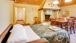 Une chambre d’hôtel chaleureuse avec un plafond en briques, un lit recouvert d’une courtepointe à motifs, une table à manger avec des chaises et un petit coin cuisine.