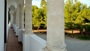 A corridor with white columns and a tiled floor, leading to a covered outdoor area with trees. - Belvilla by OYO Tramonto di Salento Grande (Torricella)