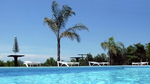 A clear blue pool with white lounge chairs and a palm tree. - Belvilla by OYO Tramonto di Salento Grande (Torricella)