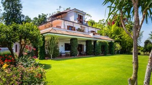 A two-story house with a covered patio, surrounded by a well-maintained lawn and various plants. - Belvilla by OYO Villa Conte (Ricadi)