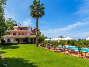 A two-story building with a pool area, surrounded by greenery and palm trees. - Belvilla by OYO Villa Conte (Ricadi)