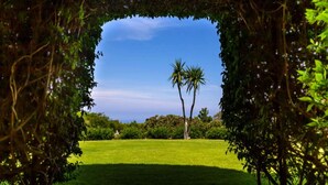 A view through a framed archway of a lush green lawn with palm trees and dense foliage. - Belvilla by OYO Villa Conte (Ricadi)
