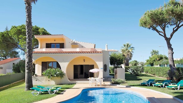 Une maison à deux étages avec une piscine, une pelouse verdoyante et des chaises longues.