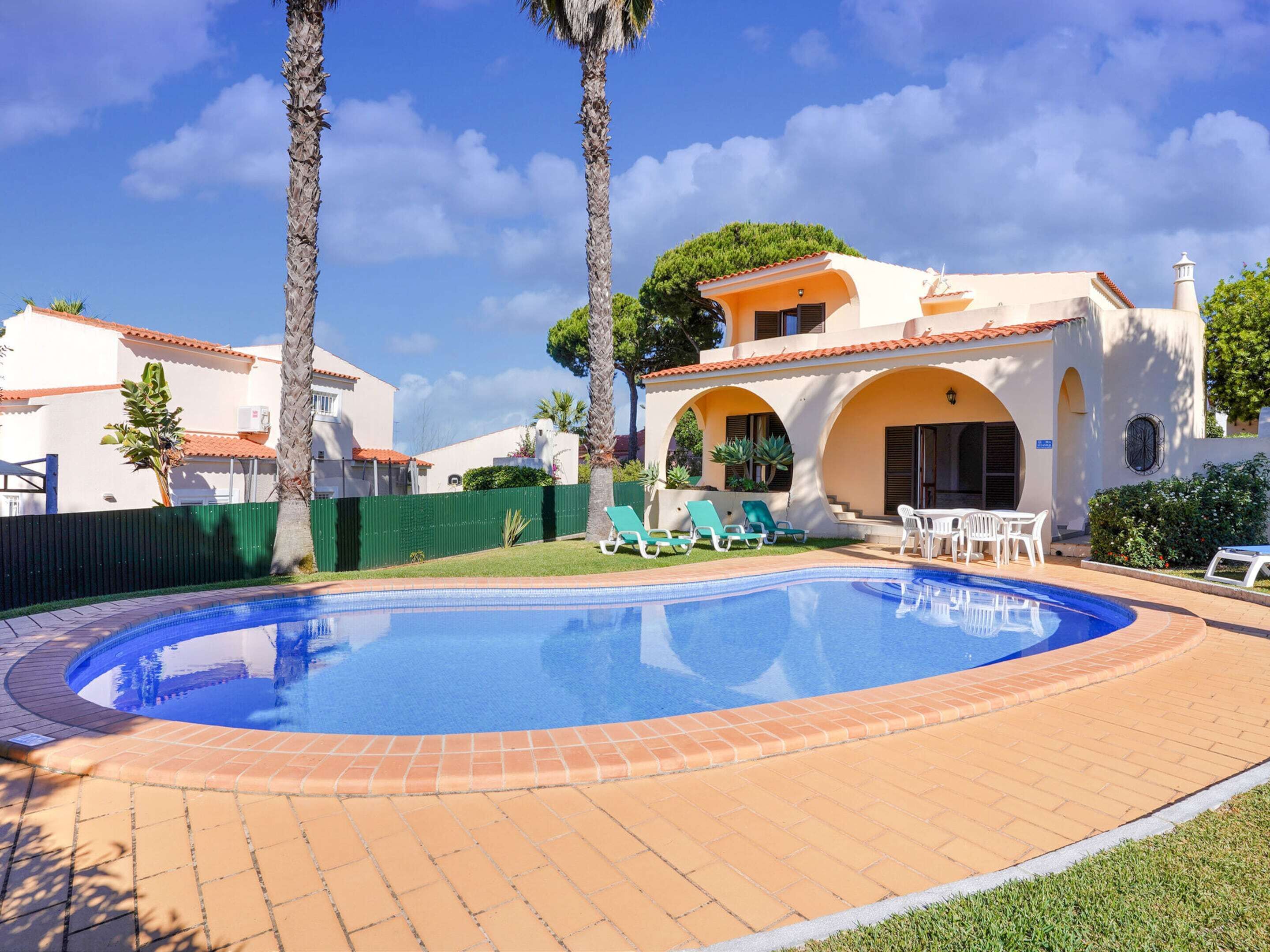 Uma piscina com espreguiçadeiras, um espaço de pátio e um edifício com telhado em azulejo.