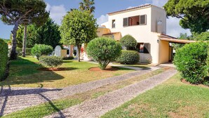 Une maison à deux étages, avec une allée pavée menant à l’entrée, entourée de pelouses bien entretenues et de divers arbres.