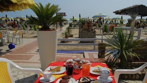 Een tafel met eten en drinken, omringd door strandstoelen en parasols, met uitzicht op het strand.