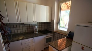 Eine kleine Küche mit weißen Schränken, einer Kaffeemaschine und einem Kühlschrank.