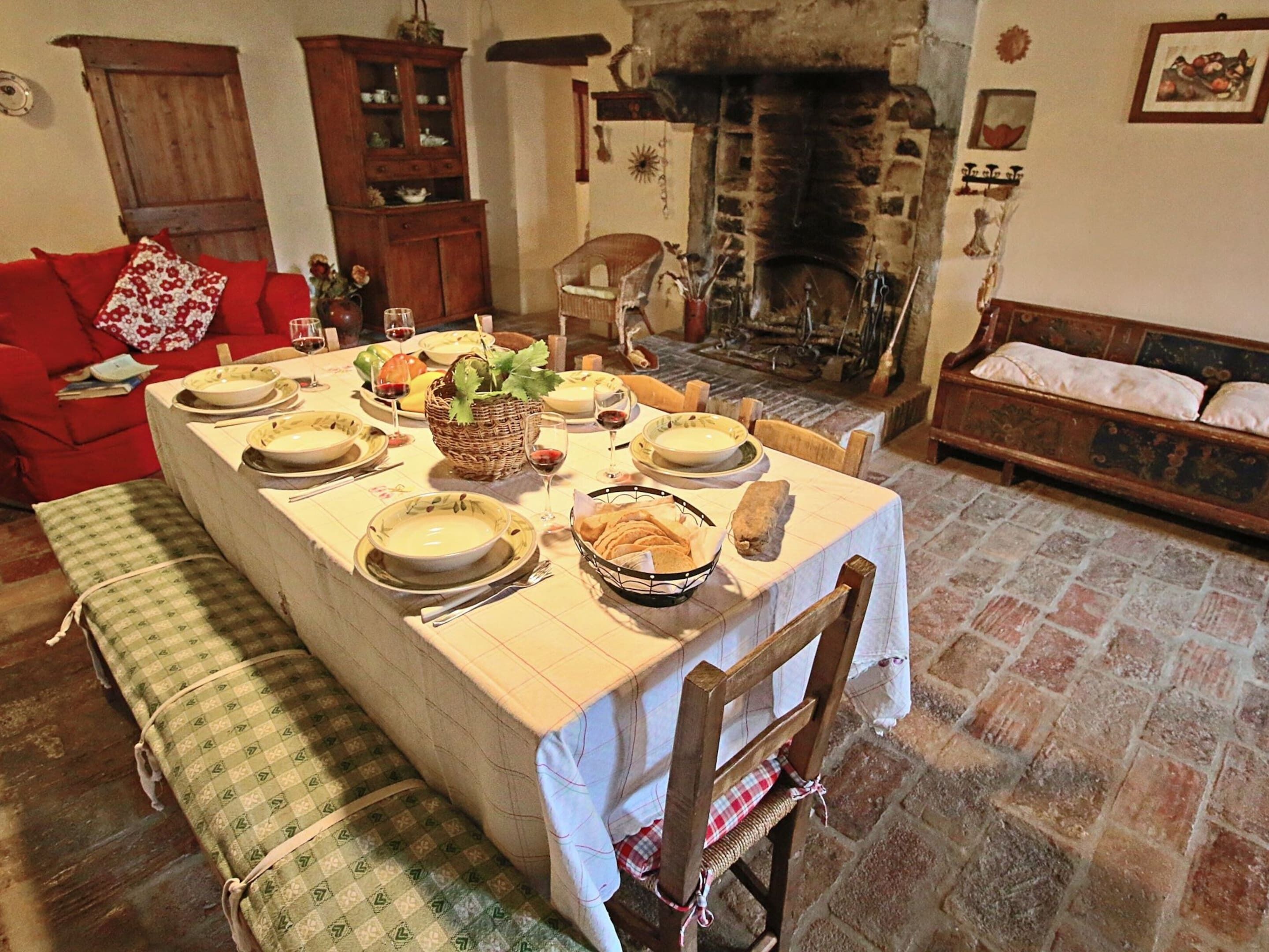 Un comedor con una mesa larga dispuesta para una comida, rodeado de mobiliario de madera y una chimenea.