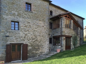 Un edificio de piedra con varias ventanas, una puerta de madera y un pequeño jardín.
