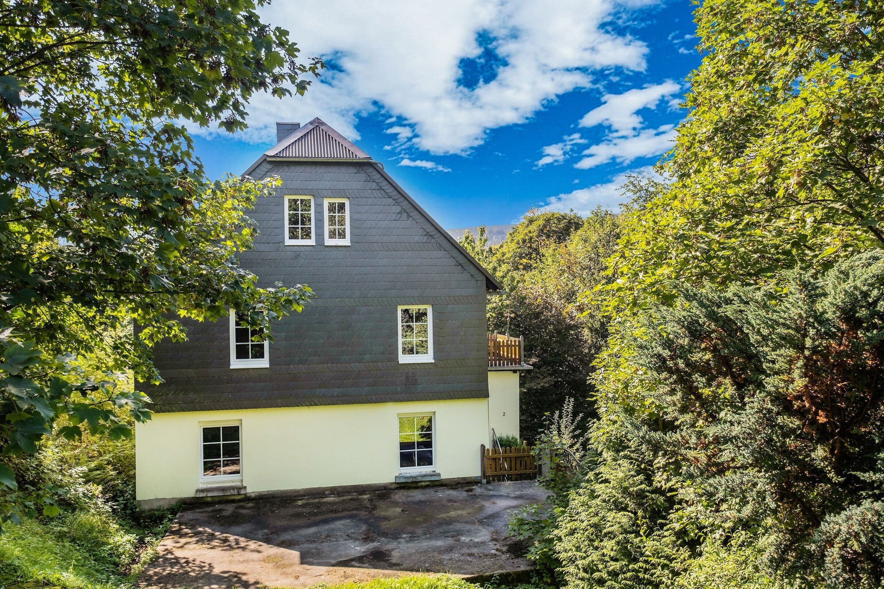 A two-story house with a sloped roof, a small porch, and a fenced yard.