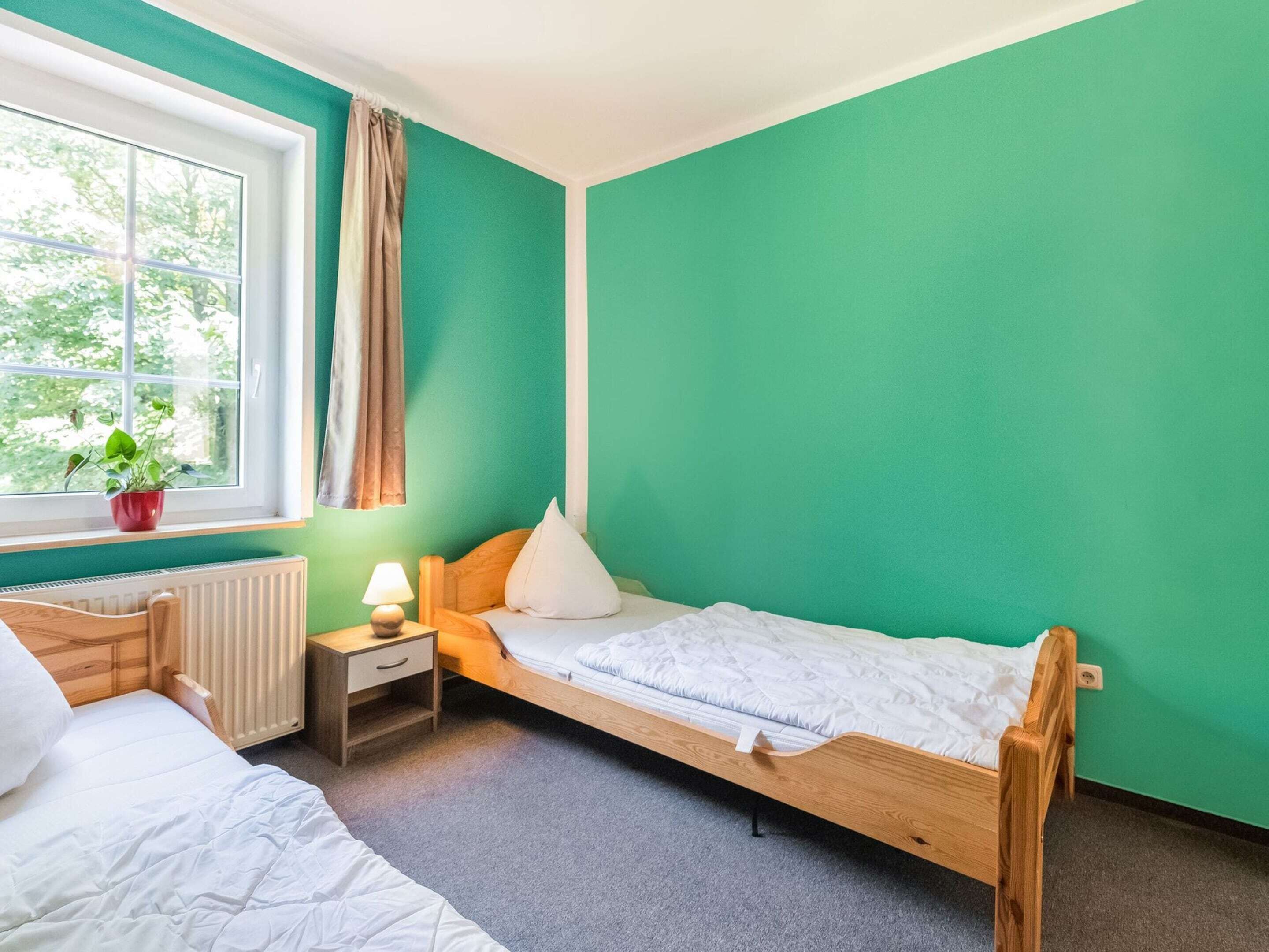 A room with a bed, a nightstand, a window with curtains, and a radiator.