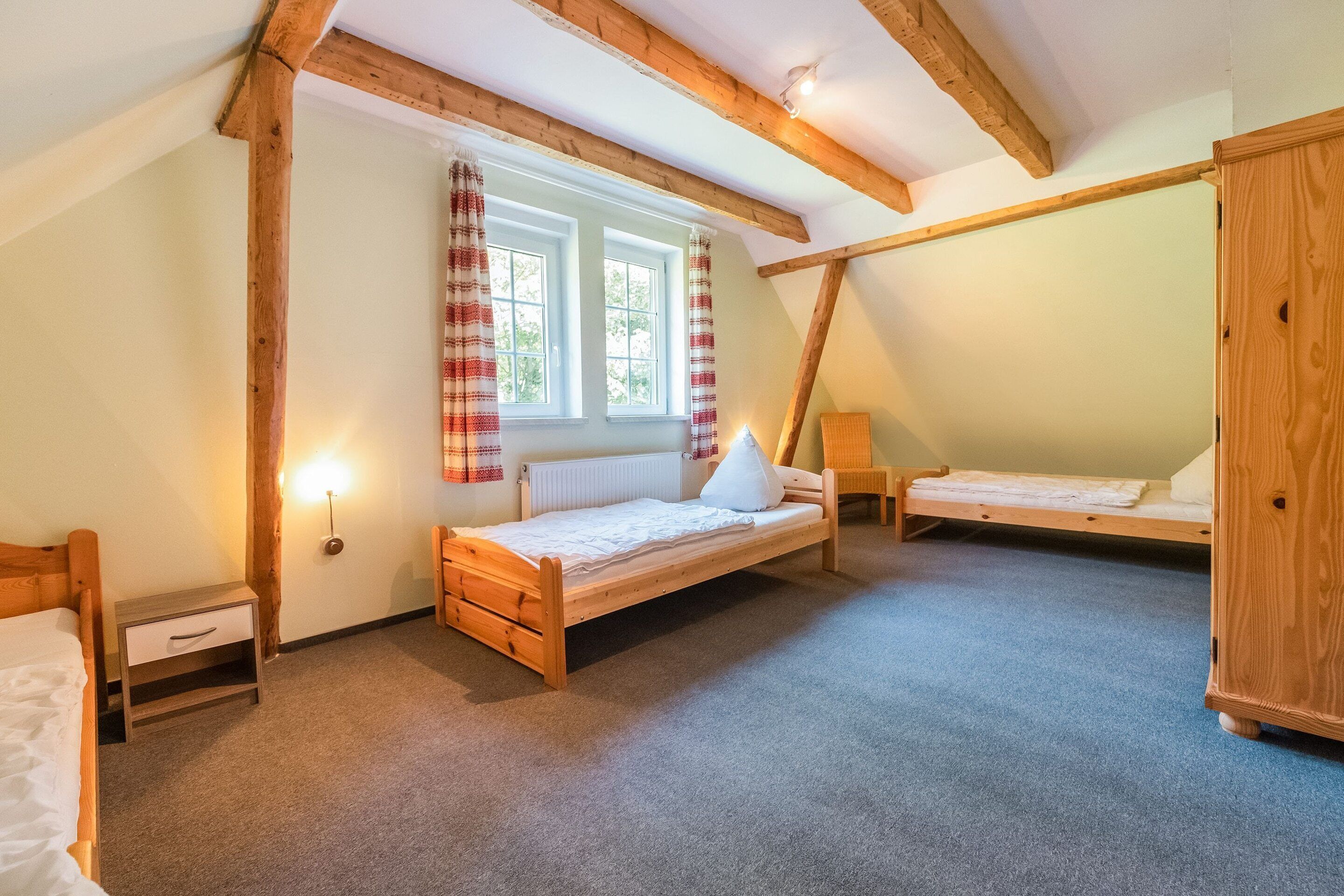A cozy attic bedroom with two wooden beds, a nightstand, and a wardrobe.