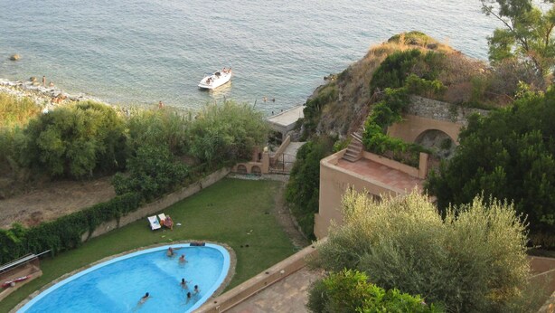 A swimming pool with people, a boat on the water, and a view of the sea. - Mansion in Capo Vaticano With Sea Views (Ricadi)