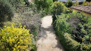 A gravel path flanked by dense greenery and a building with a tiled roof. - Holiday Home in Lido di Noto Near Beach (Noto)