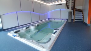 Un spa moderno con una bañera de hidromasaje grande, una escalera de madera y un piso con motas azules.