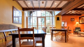 Comedor con mesas y sillas de madera, ventanas amplias y vista a los árboles.