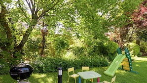 A grassy outdoor area with a barbecue grill, a table with chairs, and a children's play structure. - Captivating Holiday Home in Malmedy With Sauna (Malmedy)