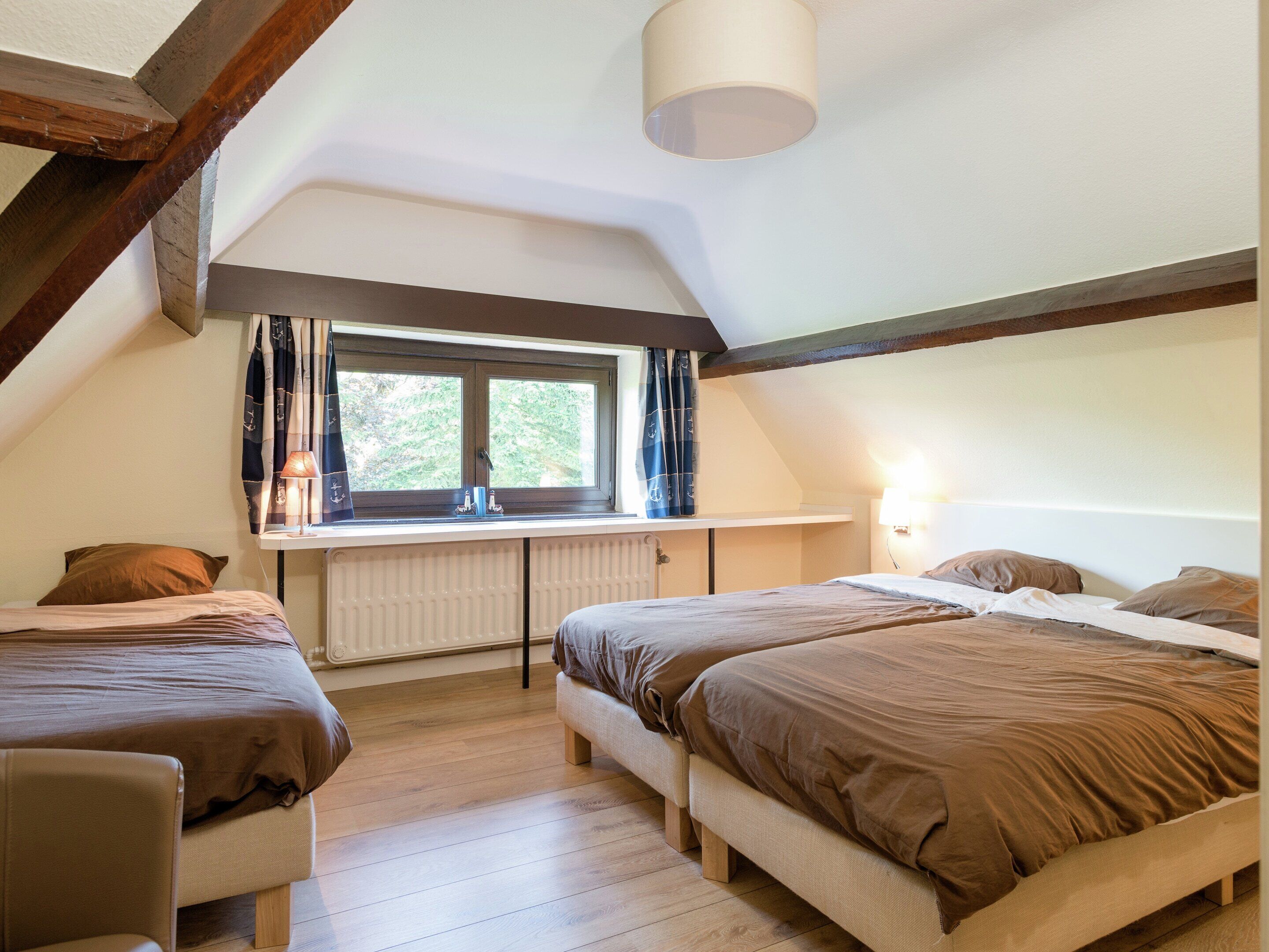 A bedroom with two beds, a window with curtains, a radiator, and a lamp.