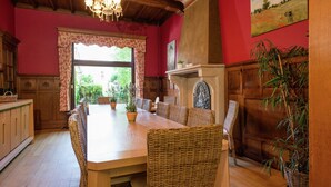 A dining area with a wooden table and wicker chairs, a chandelier, and a red wall with a painting. - Captivating Holiday Home in Malmedy With Sauna (Malmedy)