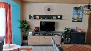 A modern living room with a flat-screen TV, wooden cabinet, and decorative items on a shelf.