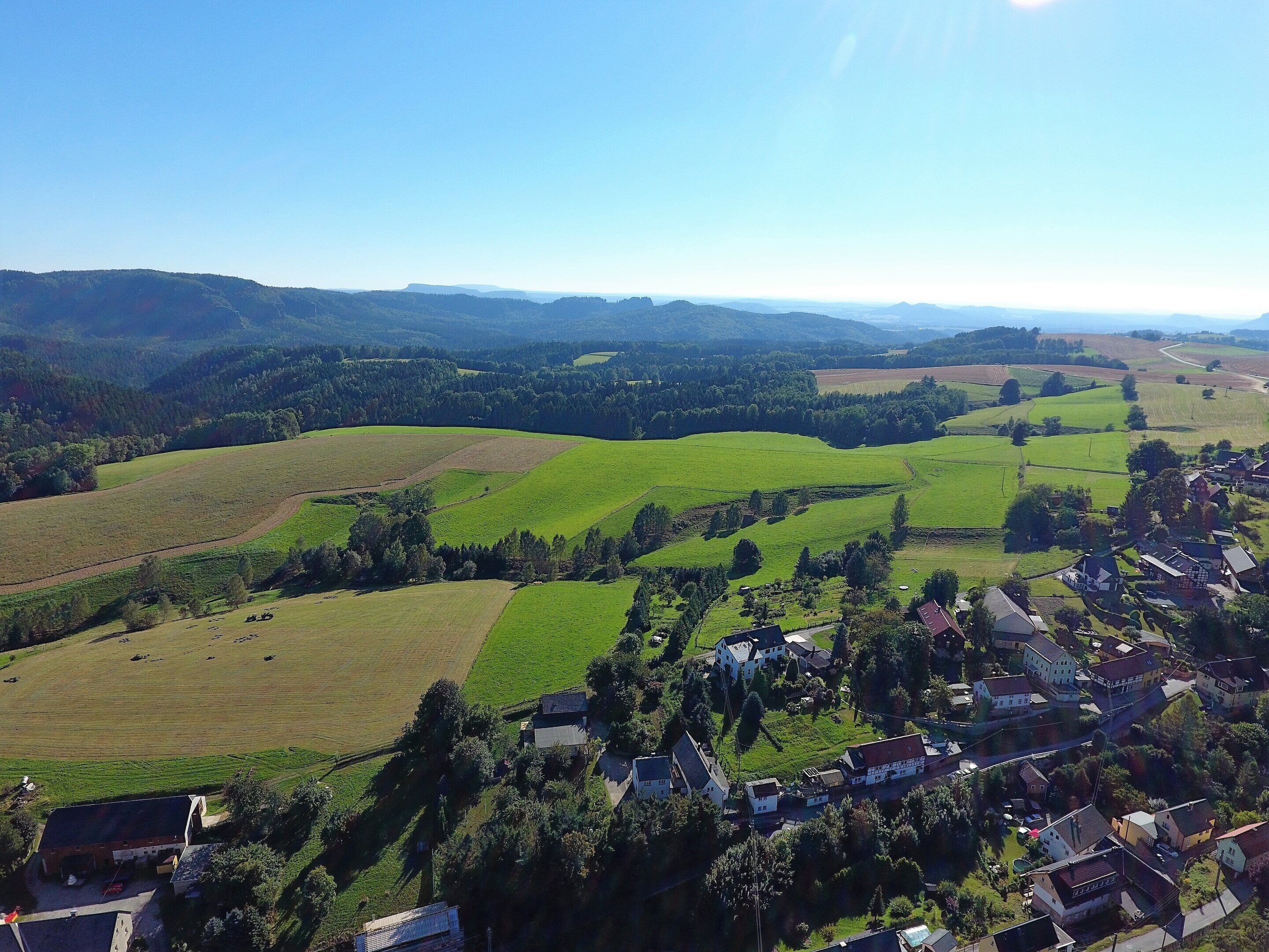 A rural landscape with rolling green fields, a small village with houses, and distant hills.