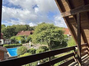 A wooden balcony overlooking a swimming pool, a garden, and a residential area with houses and trees. - Holiday Apartment in the Teutoburg Forest (Brakel)