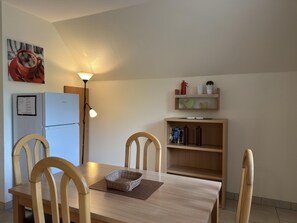 Un coin repas comprenant une table, des chaises, une lampe, un réfrigérateur et une étagère avec des objets décoratifs.