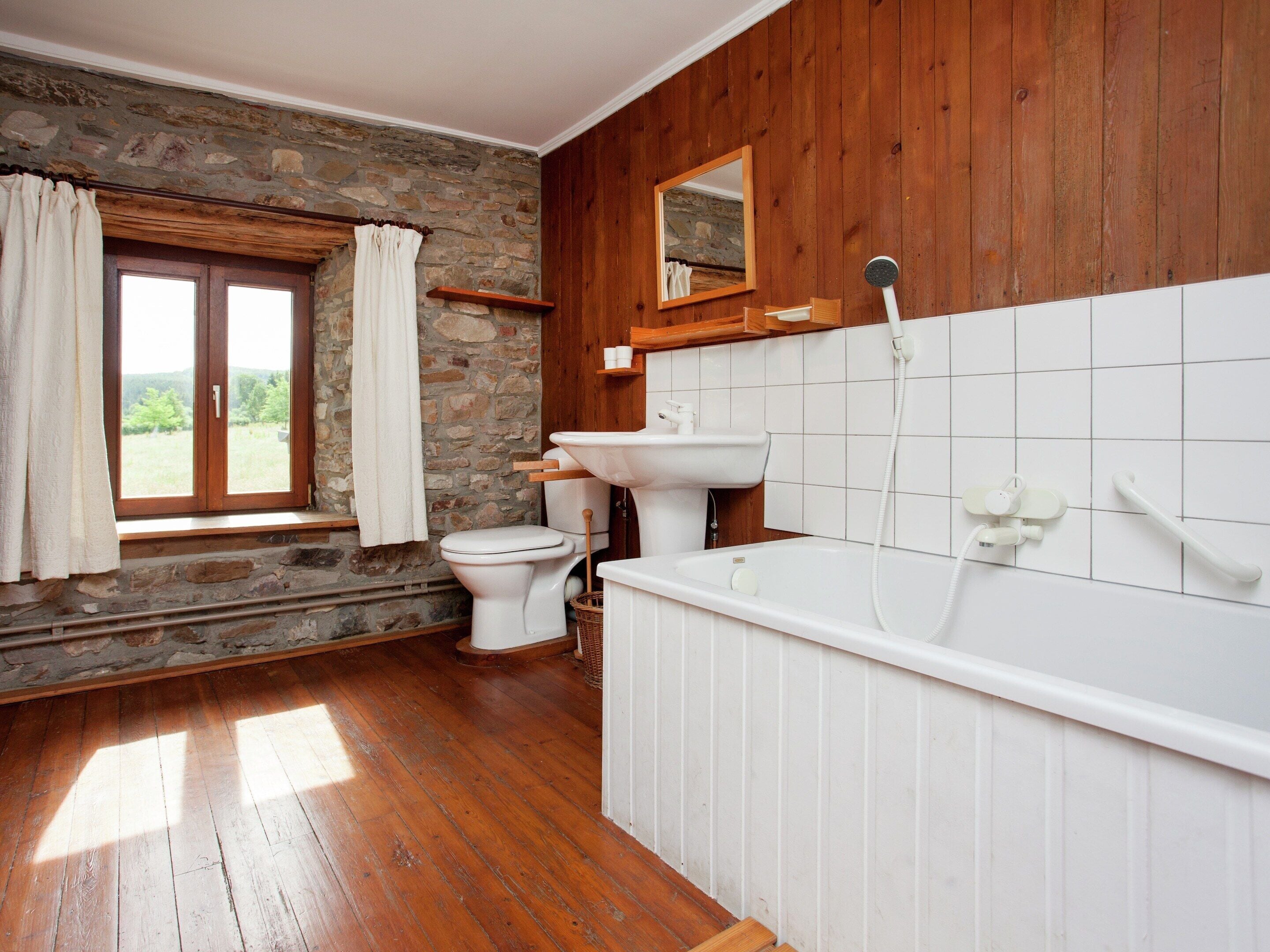 A bathroom with a stone wall, wooden paneling, a toilet, a sink, and a bathtub.